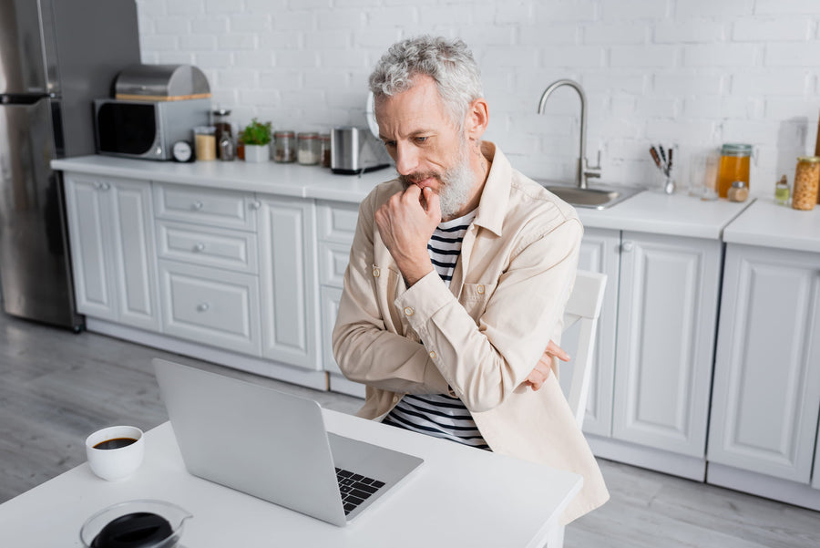 Thoughtful middle-aged man reviewing information on his laptop at home